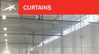 Indoor sports hall with large transparent divider curtains suspended from the ceiling. A red banner at the top reads “CURTAINS” with HiTech’s logo.