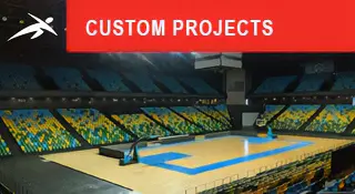 Empty indoor sports arena with a large timber floor court and coloured seating. A red banner at the top reads “CUSTOM PROJECTS” with HiTech’s logo.
