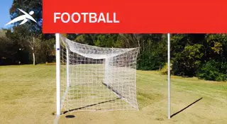 Outdoor football (soccer) goal with net set up on a grassy field surrounded by trees. A red banner at the top reads “FOOTBALL” with HiTech’s logo.