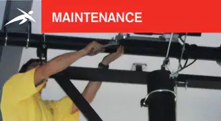 Technician in a yellow shirt performing maintenance on overhead sports equipment. A red banner at the top reads “MAINTENANCE” with HiTech’s logo.