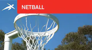 Outdoor netball hoop with a white ring and net set against a blue sky and tree backdrop. A red banner at the top reads “NETBALL” with HiTech’s logo.